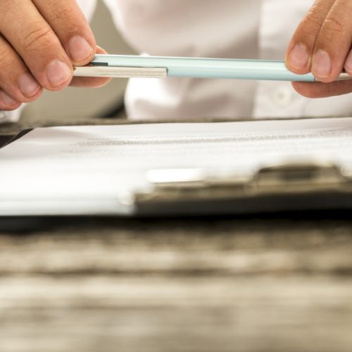 Closeup view of male hands holding pencil over paperwork on clip